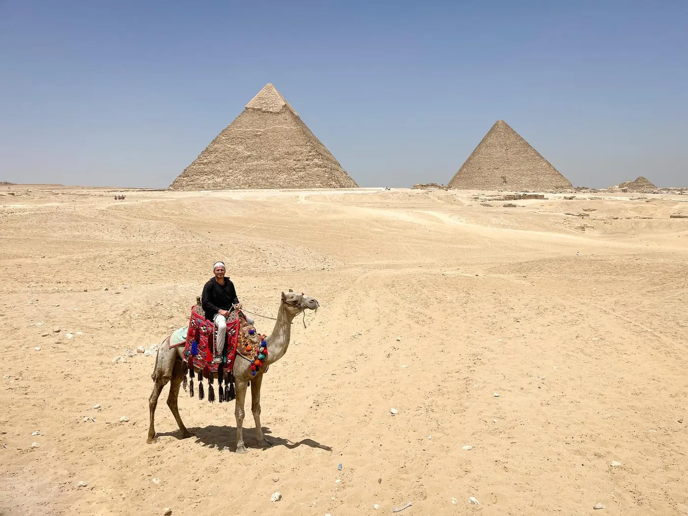 Danny riding a camel before the pyramids