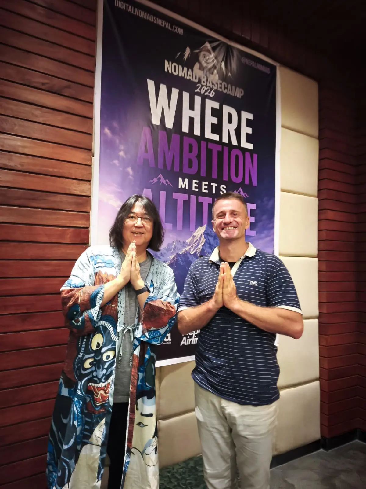 Danny at the Nomad Basecamp summit beside a 'Where ambition meets altitude' banner